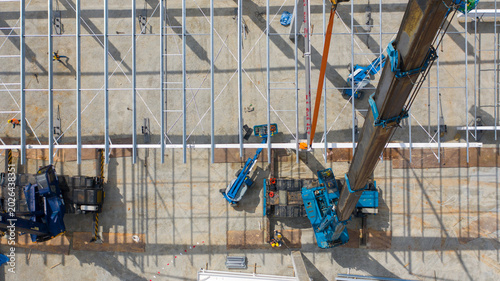 Foto Aerial View of Construction Site: A high-angle view captures an active construction site with a crane lifting steel beams, showcasing industrial progress and building development