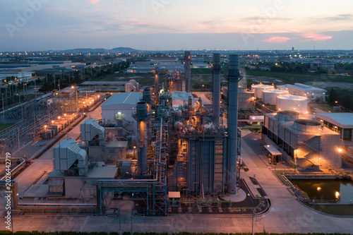 Obraz na płótnie Industrial Powerhouse at Dusk: An illuminated industrial complex, likely a power generation facility, stands against the twilight sky, showcasing a network of pipes, stacks, and cooling towers