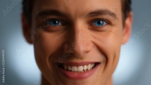 Close up of a young mans face with striking blue eyes smiling.
