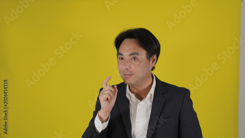 Photos Confident Asian Businessman Gesturing While Speaking Against a Yellow Background