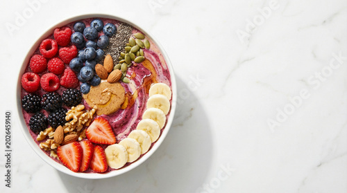 Close-up top view of a purple berry smoothie bowl served with a dollop of creamy peanut butter, sliced bananas, and pumpkin seeds.