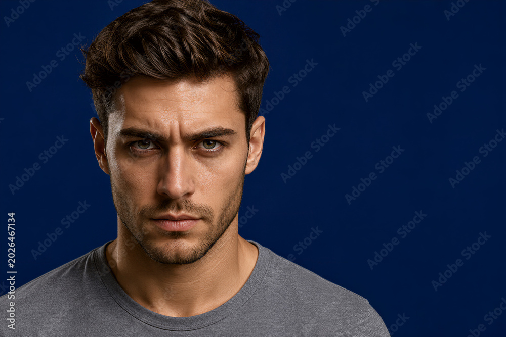 Obraz premium Serious Young Man Portrait on Dark Blue Background as Masculine Confidence and Modern Lifestyle Branding Concept 