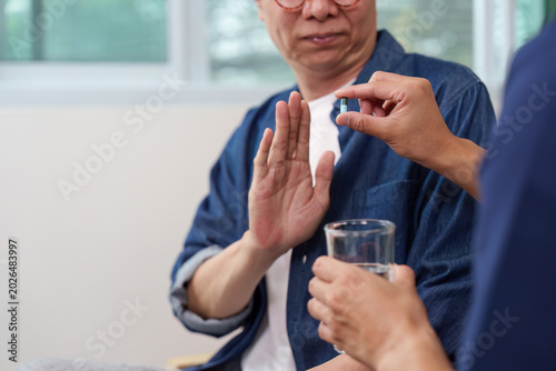 Asian senior man patient refusing medication from caregiver at home