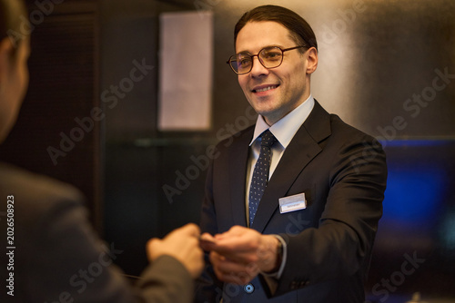 Caucasian hotel receptionist handing key card to guest during check in, supporting hospitality service and customer care. Useful for travel booking, tourism, concierge marketing