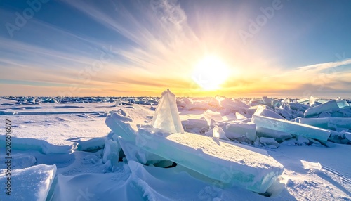 A bright, sunlit landscape of frozen water and snow. Ice chunks reflect the sun's warm light against a clear blue sky