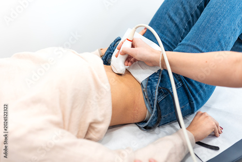 Obraz na plátně Close up of doctor performing ultrasound scan on belly of female patient in hospital