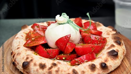 Burrata cheese is spread on focaccia bread and topped with tomatoes.