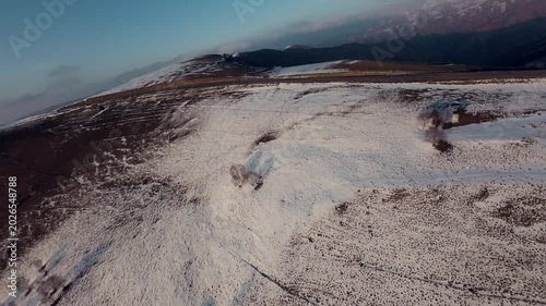 Aerial view of snow-covered mountains and winding road during low flight