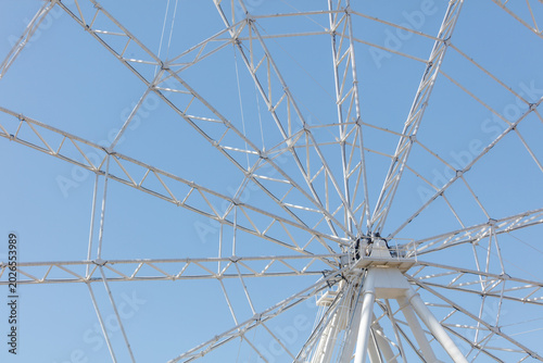 Low-angle view of giant white Ferris wheel under bright blue sky