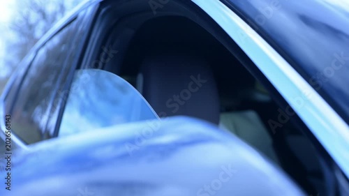 Lowering a car door window. A modern car window reflects clear blue skies and green leaves, capturing a tranquil moment of nature meeting sleek automobile design under bright sunlight.