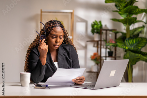 Photos African corporate businesswoman concentrating on documents and laptop in a moder