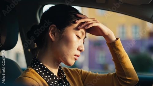 Young Asian woman experiencing headache or stress while sitting in a car, feeling unwell and exhausted.