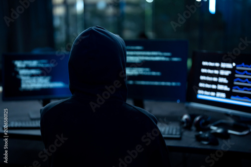 Canvastavla Male computer hacker in black hoodie typing code on computer in a dark room with light reflection on glasses