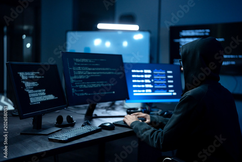 Obraz na plátně Male computer hacker in black hoodie typing code on computer in a dark room with light reflection on glasses