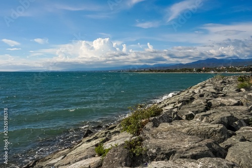 Calm sea meets rugged rocks under bright blue sky