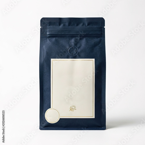 A dark navy blue coffee bean packaging pouch with a blank rectangular label and a small circular sticker, featuring a minimalist gold botanical isolated on a clean white studio background