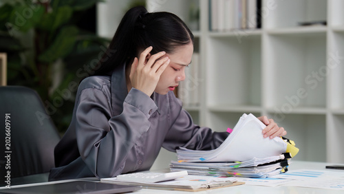 Foto Stressed Asian businesswoman overwhelmed by paperwork in office