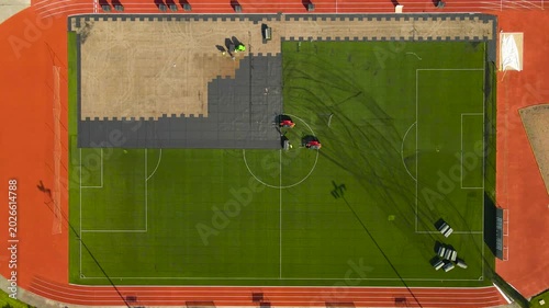 Top down aerial view of construction workers installing a new artificial turf on a soccer pitch surrounded by a running track
