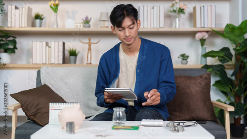 Tableau sur toile Asian man budgeting personal finance and saving money with piggy bank at home