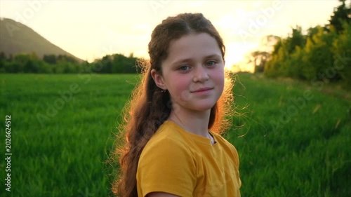 Portrait of smiling charming pretty preteen girl in park at summer warm day. Adorable happy child is dreaming looking at camera. Children day. Childhood and nature concept