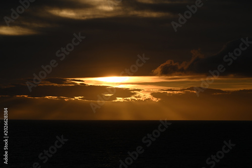 Dramatic Golden Sunset over the Ocean Horizon with Sun Rays Piercing Through Dark Clouds