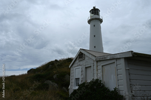Historic White Lighthouse Tower Rising Behind an Old Weathered Wooden Shed Under Cloudy Skies