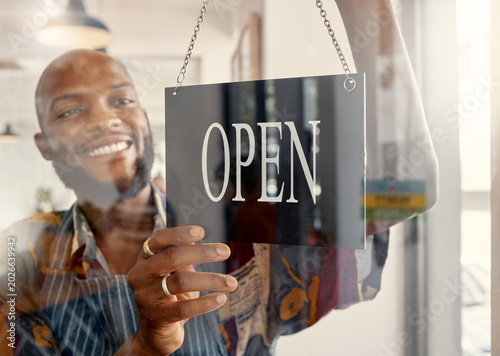 Happy, man and window in restaurant with open sign, small business owner or ready for customer service. Black person, smile and entrepreneur in cafe with welcome board, pride and glass door entrance.