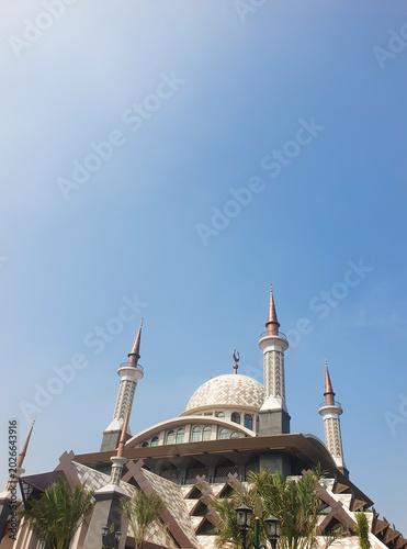 Foto A striking view of a modern mosque featuring a patterned central dome, sharp spires, and traditional crescent symbols against a blue sky