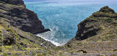 Tableau sur toile Rocky coastline with dark volcanic rocks and clear blue ocean waves lapping agai