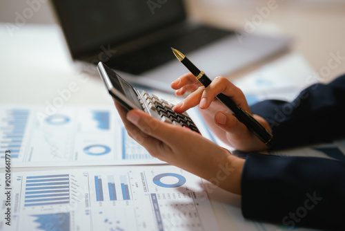 Business professional analyzing financial charts and using calculator for accounting, budgeting, and corporate financial planning at office desk.