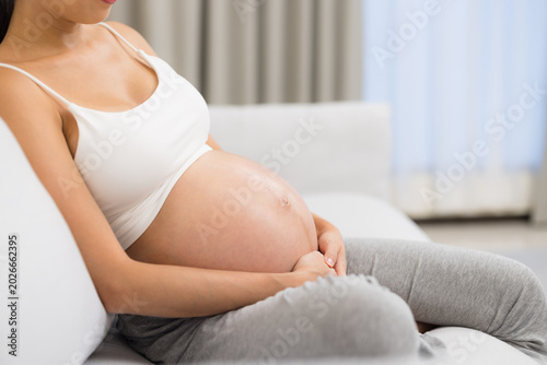 Bild auf Leinwand Pregnant woman resting on sofa gently holding her belly at home