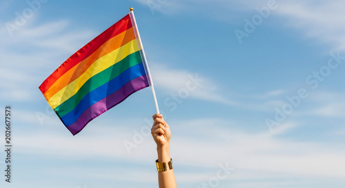 Rainbow flag waving against a blue sky with clouds, symbolizing pride, diversity, and equality, representing a celebration of identity and freedom