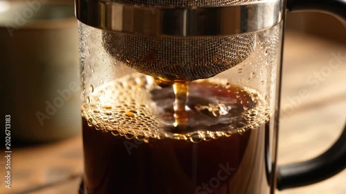 Steam rises gracefully as dark coffee flows through the mesh of a French press. The rich aroma fills the kitchen, creating an atmosphere of cozy comfort and anticipation.