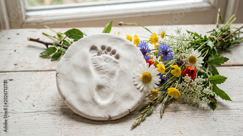 Baby footprint impression on clay with wildflowers on wooden table  