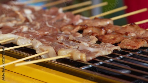 The shot of a cook grill Moo Ping or grilled pork skewers in Thai style on the yellow electric barbeque grill at the restaurant.