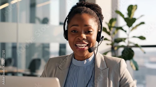 Smiling Black woman wearing a headset and suit jacket, working in a modern office environment.
