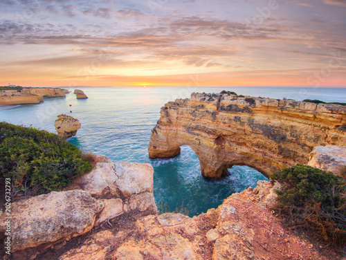 Sunrise at Praia da Marinha beach in Algarve, Portugal, with ocean cliffs, sea stacks and open sea and rock arches.
