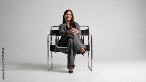 Portrait of a cheerful young businesswoman sitting in a chair against white background.