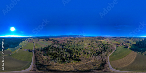 Aerial view of the rural landscape in the Seeland District featuring dense forests and agricultural fields under a clear blue sky Grossaffoltern, Bern, Switzerland.