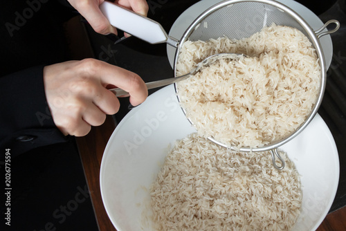 Bild auf Leinwand spoon helps transfer wet rinsed rice from a sieve into a white bowl, showing a p