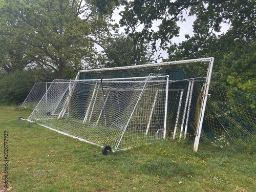 Stacked soccer goals rest on a grassy field, awaiting their next match under the open sky.