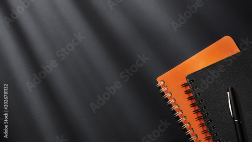 Fotografía Orange and black spiral notebooks with pen on dark textured background with dramatic lighting