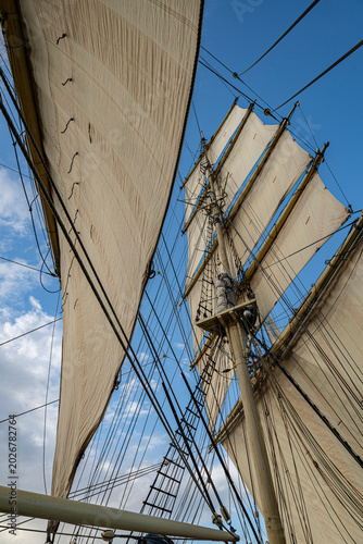 Low angle view of traditional tall ship showing foremast and mainmast with white sails set against sky