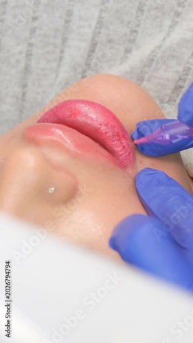 Close-up of a cosmetologist tattooing pink pigment on a woman's lips in a beauty salon