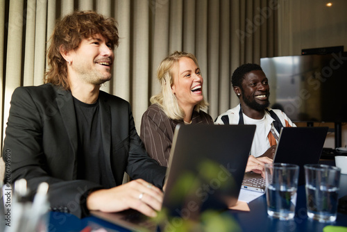 Happy male and female entrepreneurs laughing in business meeting