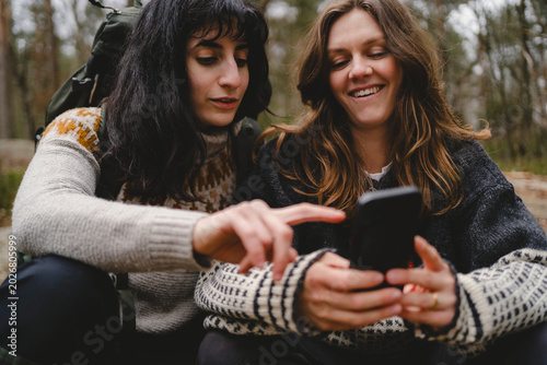 Female friends surfing on smart phone while spending leisure time in forest