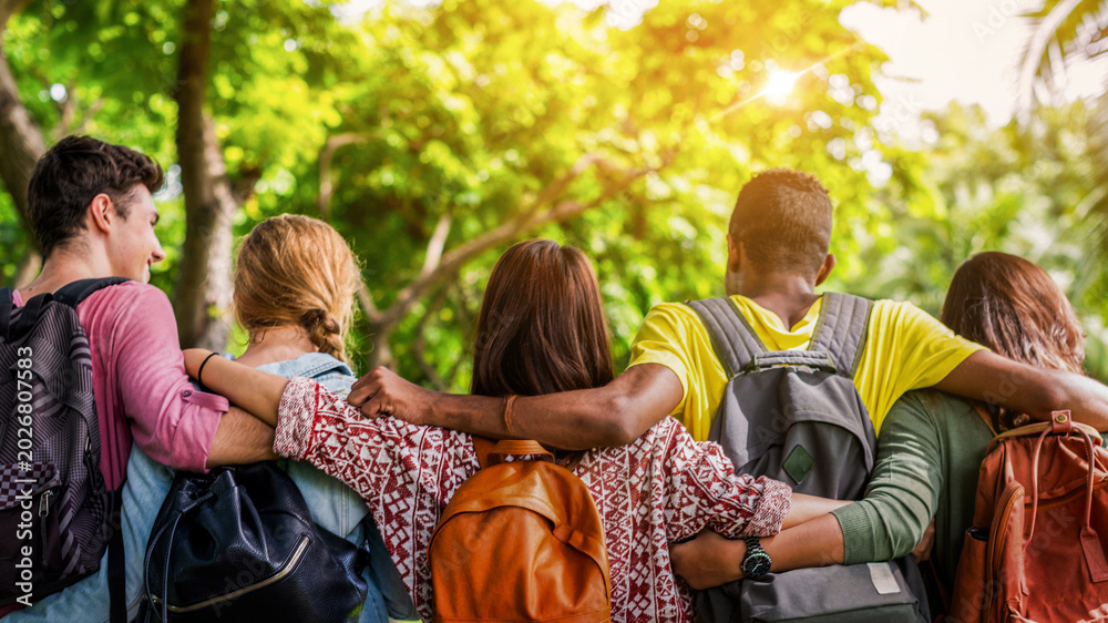 Fototapeta premium Diverse group of friends with backpacks, arms around each other outdoors.
