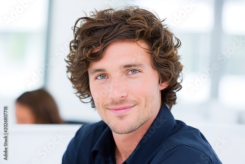 A smiling young man with curly hair in a modern office setting