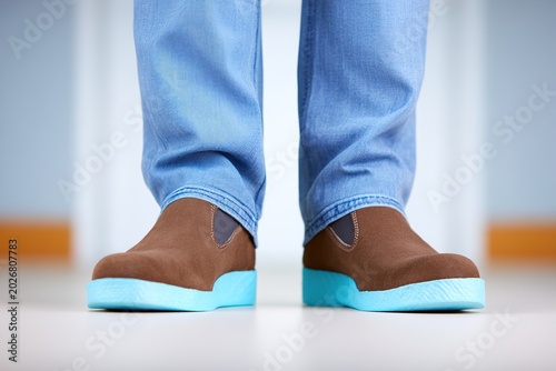 A person wearing brown shoes with blue soles and light blue jeans
