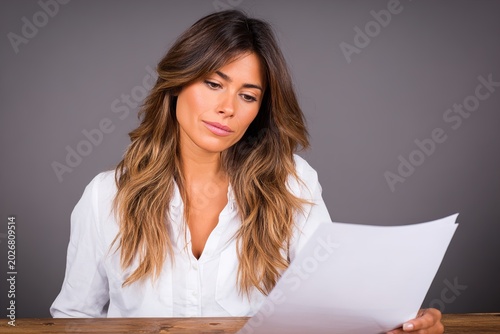 A young businesswoman reviewing documents at a wooden desk in a modern office
